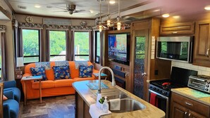 A compact RV kitchen with a central island, a dining area with a sofa, and a TV mounted on the wall. - Ocean Front with Dock, Key Largo, FL., Pirate's Cove (Key Largo)