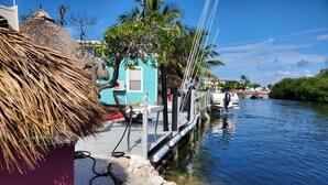 A dock with a thatched roof structure, a small boat, and a blue building with a white door. - Ocean Front with Dock, Key Largo, FL., Pirate's Cove (Key Largo)