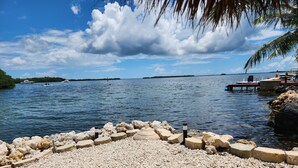 A pebbled beach with a rocky breakwater and a dock extending into calm waters. - Ocean Front with Dock, Key Largo, FL., Pirate's Cove (Key Largo)