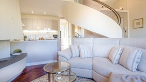 Un salon moderne avec un escalier à volutes, un canapé, une table basse en verre et une cuisine en arrière-plan.