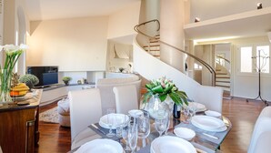 Un espace repas avec une longue table dressée pour le repas, un escalier et un coin salon avec un canapé et un téléviseur.