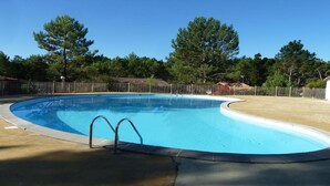 A clear blue swimming pool with a metal ladder, surrounded by a fenced area and trees. - Vacation home under the pines (moliets et maa)