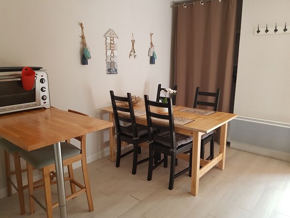 A dining area with a wooden table, four chairs, a red kettle, a toaster oven, and wall decorations.