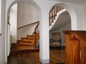 Un interior espacioso con una escalera de madera, un sillón floral y un banco de madera.