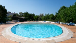 Piscina com água azul, rodeada por espreguiçadeiras e um deck revestido com azulejos.