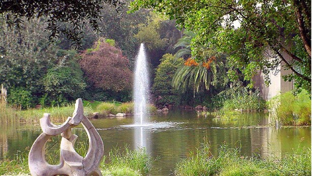 Um parque com uma fonte, uma escultura e um lago.