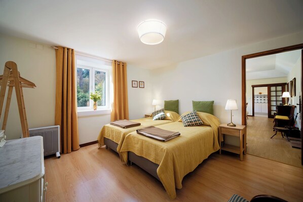 A hotel room with two beds, a wooden dresser, a radiator, and a window with curtains.