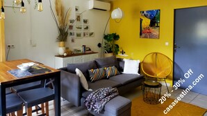 Un salon moderne avec un canapé, une table à manger et des chaises. On y trouve un mur jaune orné d’un tableau, un climatiseur blanc et une porte.