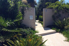 Un sendero conduce a la entrada de una villa rodeada de abundante vegetación y un muro de piedra.