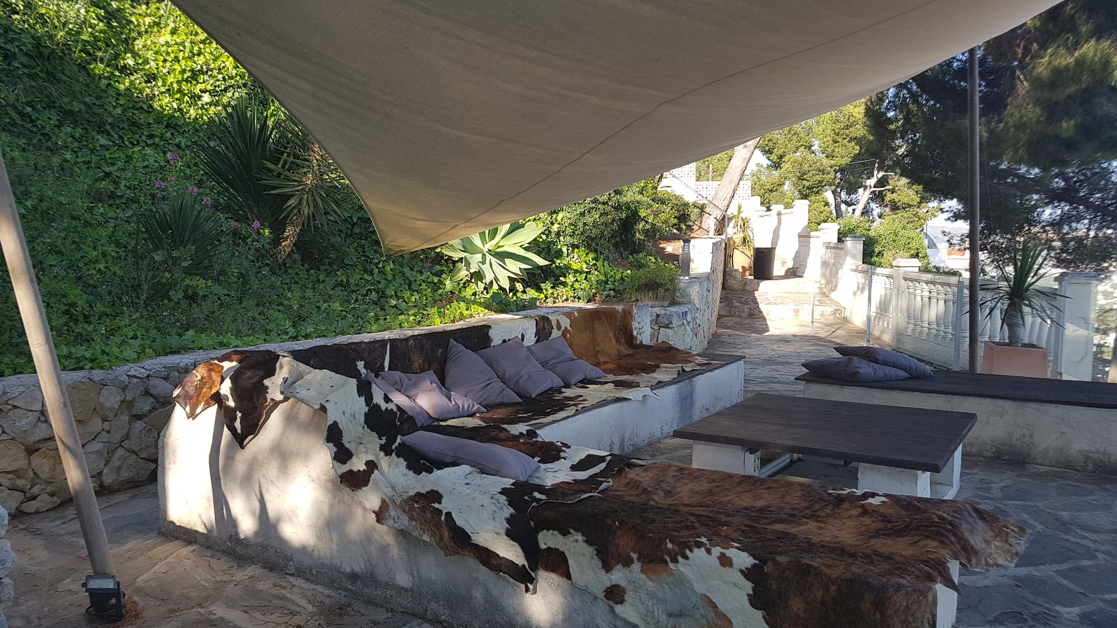 A rustic outdoor seating area with a cowhide sofa and cushions, surrounded by greenery and stone walls.