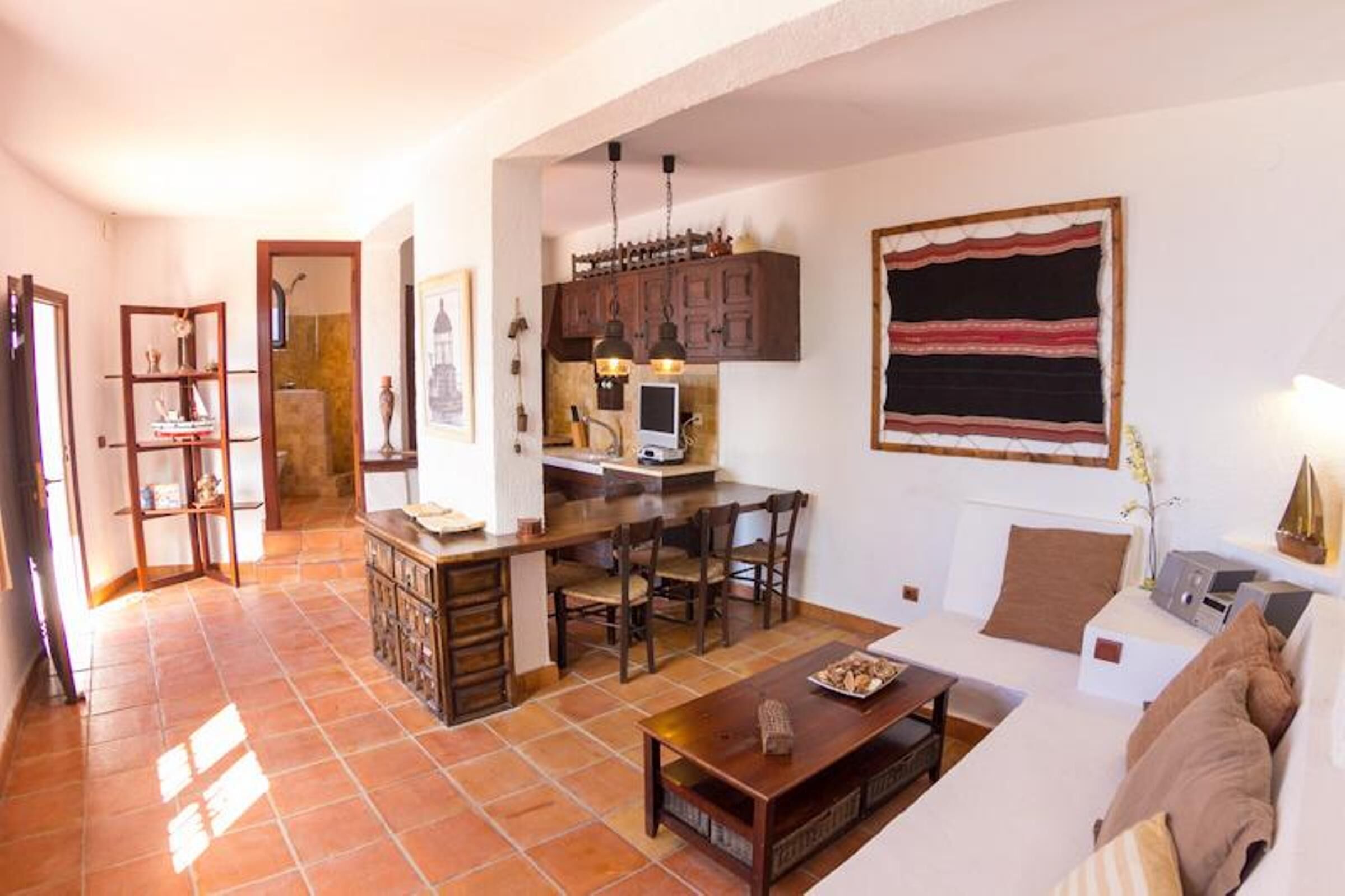 Uma sala de estar aconchegante com sofá, mesa de centro e área de jantar com cadeiras e mesa. Há também uma cozinha com armários e luminária pendente.