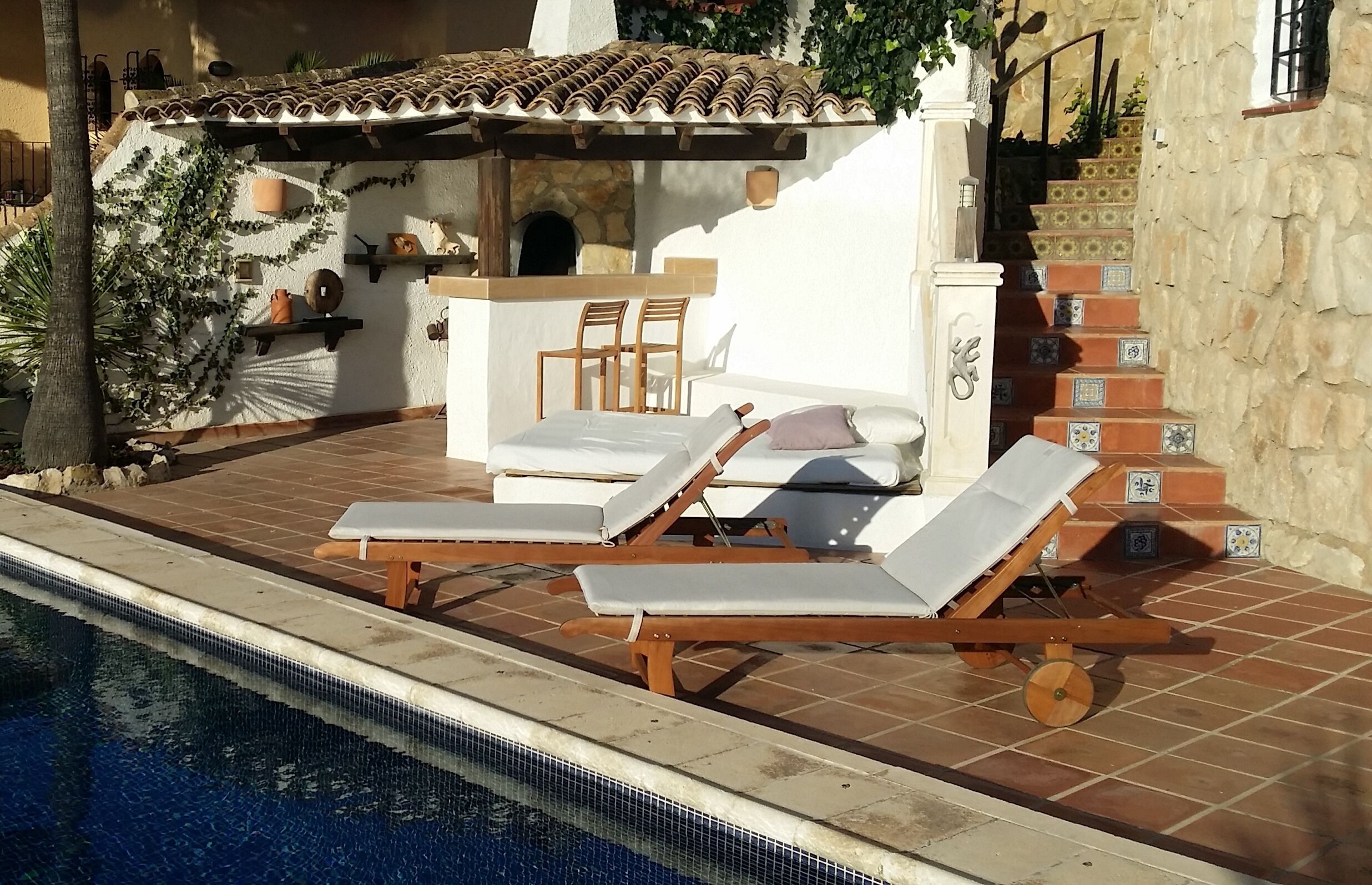A poolside area with lounge chairs, a small table, and a staircase leading to an upper level.