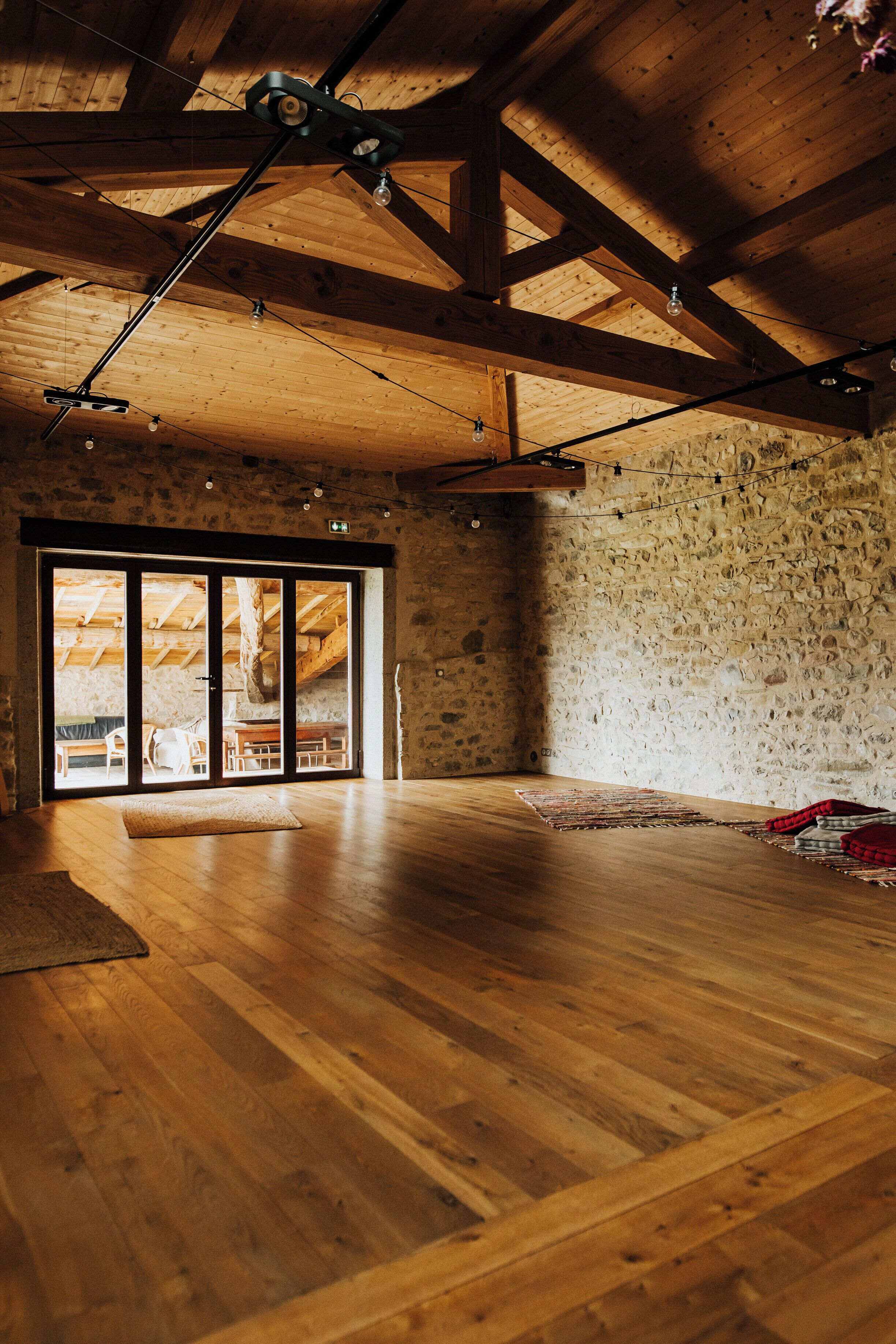 A spacious room with wooden floors, a stone wall, and a large sliding glass door leading to another area.