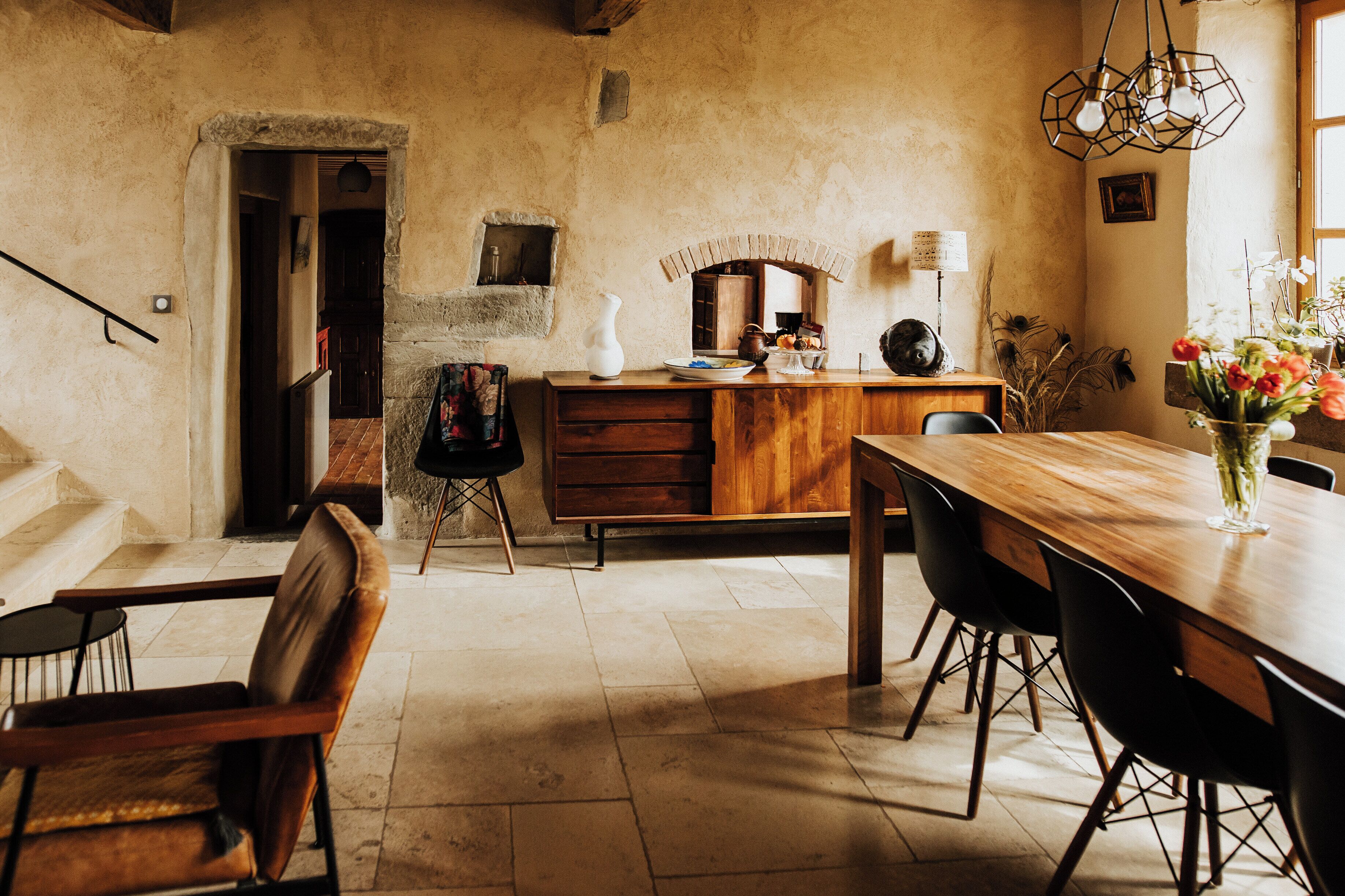 A rustic dining area with a wooden table, chairs, and a vase of flowers.