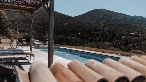 Un espace aménagé au bord de la piscine, avec des chaises longues et une terrasse en bois offrant une vue sur la montagne.