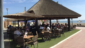 An outdoor seating area with thatched umbrellas and wicker furniture, overlooking a beach.