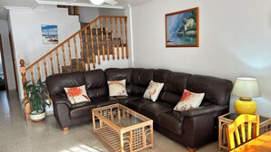 A living room with a brown leather sofa, a glass coffee table, a wooden side table with a lamp, and a painting on the wall.