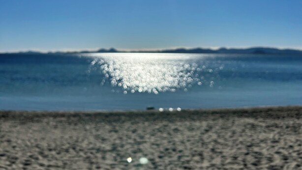A beach with a clear sky and the sun shining.