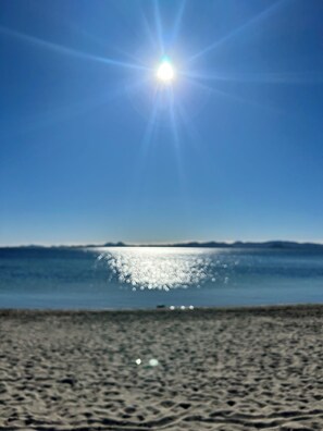 A beach with a clear sky and the sun shining.