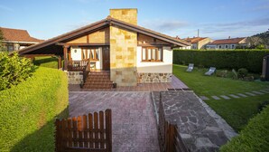 Une maison à deux étages avec une façade en pierre, une terrasse en bois et une pelouse bien entretenue.