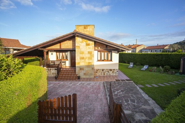 Una casa de dos pisos con fachada de piedra, una terraza de madera y un césped bien cuidado.