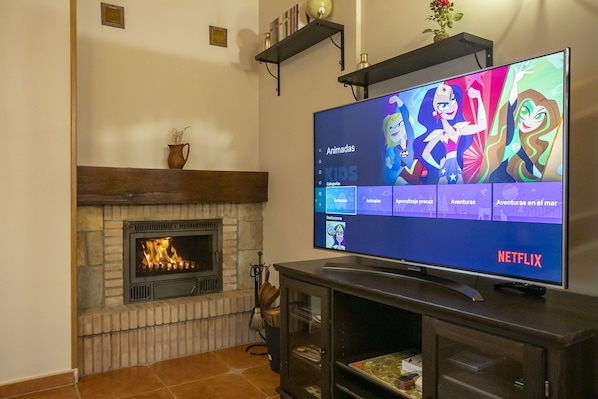 A living room with a fireplace, a flat-screen TV displaying a Netflix interface, and a shelf above the TV.