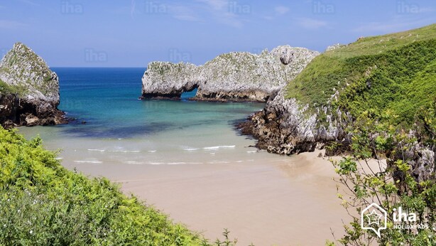 Un paysage côtier caractérisé par des formations rocheuses, une plage de sable et des eaux d’un bleu limpide.