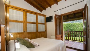 Une chambre avec un lit, une table de chevet, une télévision et un balcon donnant sur un espace verdoyant.