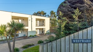 A modern two-story building with a balcony on the second floor, a wooden fence with a 'WESTWARD' sign, and a backdrop of trees and shrubs.