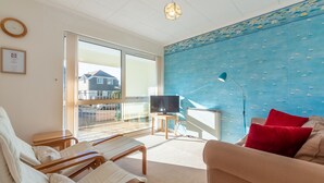 A living room with a sofa, armchairs, a TV, and a balcony with a view of houses.