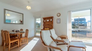 A spacious living area with a dining table, wooden chairs, a sofa set, a wooden cabinet, and a large window offering a view of the outside.