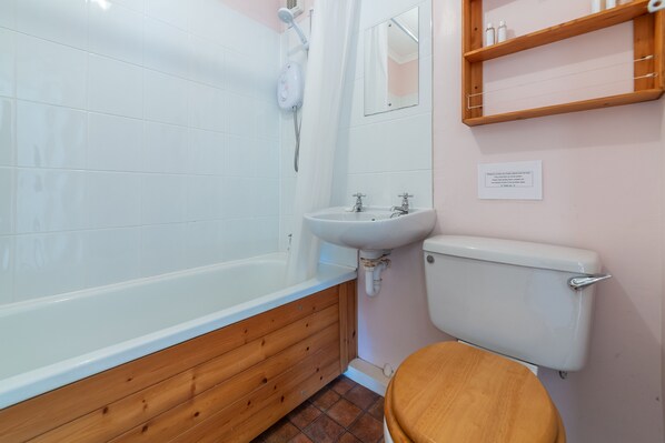 A bathroom with a wooden bathtub, a white sink, and a toilet.