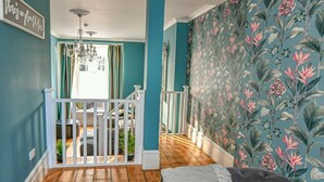 Ein Zimmer mit türkisfarbenen Wänden, Holzboden, weißer Geländer und blumigem Wandpapier.