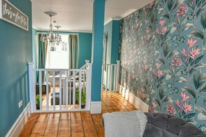 Una habitación con paredes color turquesa, piso de madera, barandal blanco y papel tapiz floral.