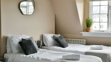 A hotel room with two beds, a mirror, a window with a plant, and a radiator.