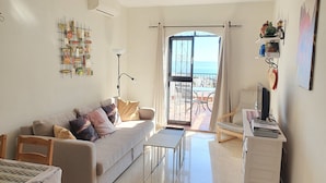 Un salon comprenant un canapé, une table basse, un téléviseur et un balcon avec vue sur la mer.