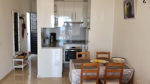 Une cuisine compacte avec des meubles blancs, un four encastré et un coin repas comprenant une table et des chaises.