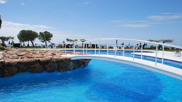 Une piscine avec un pont blanc, une eau d’un bleu cristallin et une vue sur la mer.