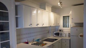 Een keuken met witte kasten, een magnetron, een spoelbak en een koelkast.