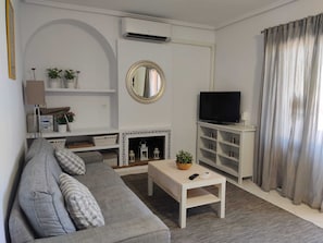 Ein Wohnzimmer mit einer Couch, einem Fernseher, einem Kamin und einem Spiegel.