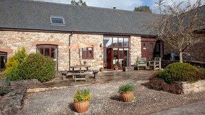 A stone building with a tiled roof, a wooden bench, and potted plants in the foreground. - Gold Award winning cottage- with indoor heated pool and games area- pet friendly (Totnes)