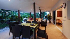 A dining area with a table set for four, surrounded by chairs, with a view of lush greenery outside. - Beachfront Resort: Villa 4-bdr, very spacious, only 20m to the beach. (Maenam)