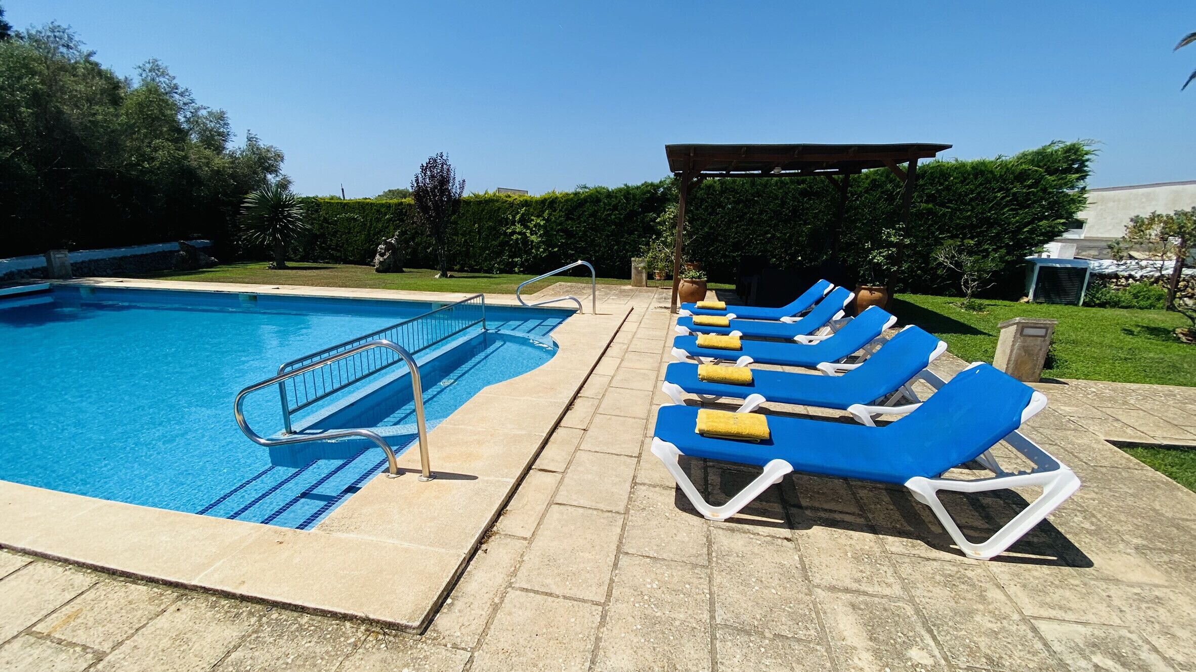 A swimming pool with blue and white lounge chairs and a covered area.