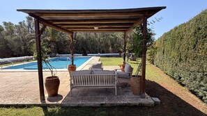A covered outdoor seating area with a pool, surrounded by greenery.