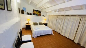 Een slaapkamer met een bed, twee nachtkastjes, een stoel, een schilderij aan de muur en een gordijn.