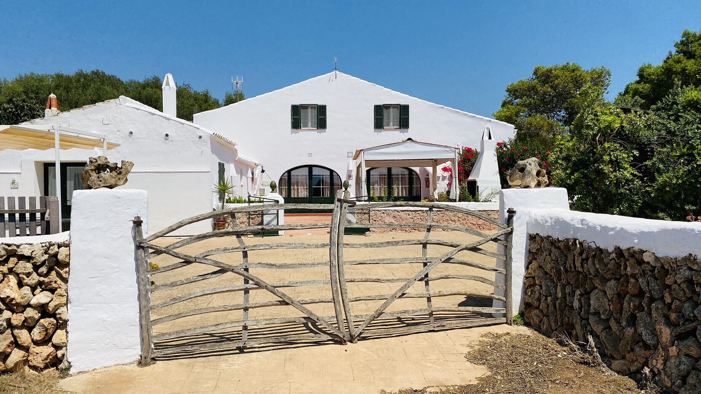 A white villa with a stone wall and a metal gate.