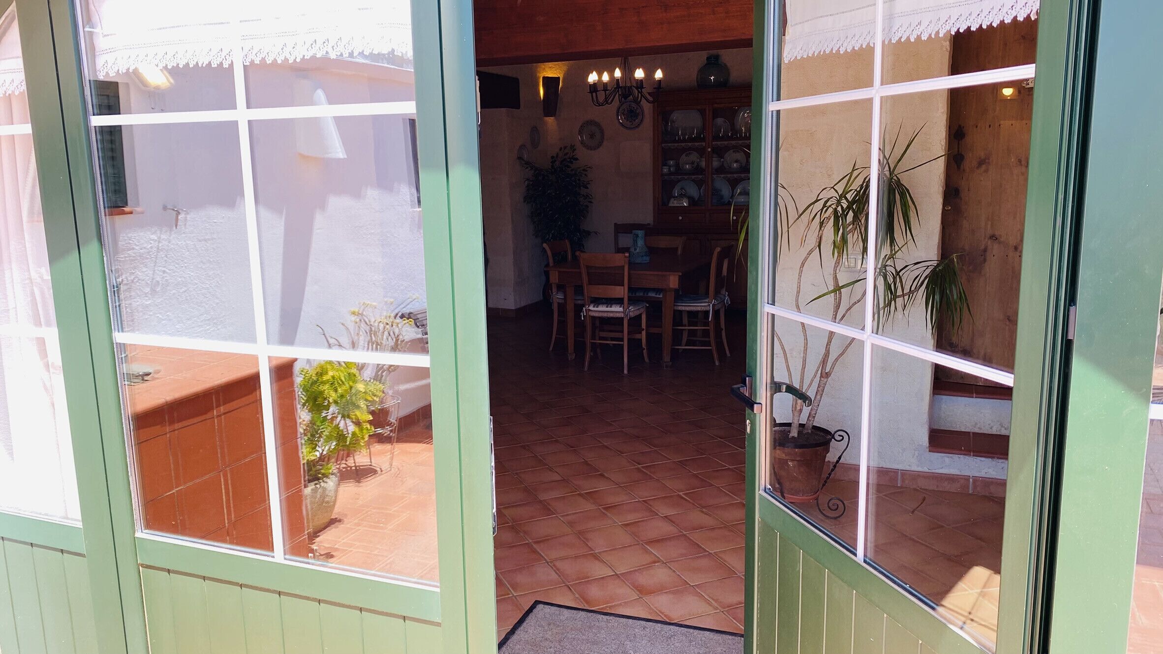 Un patio con suelo de baldosas, una mesa de madera, sillas y plantas en macetas.