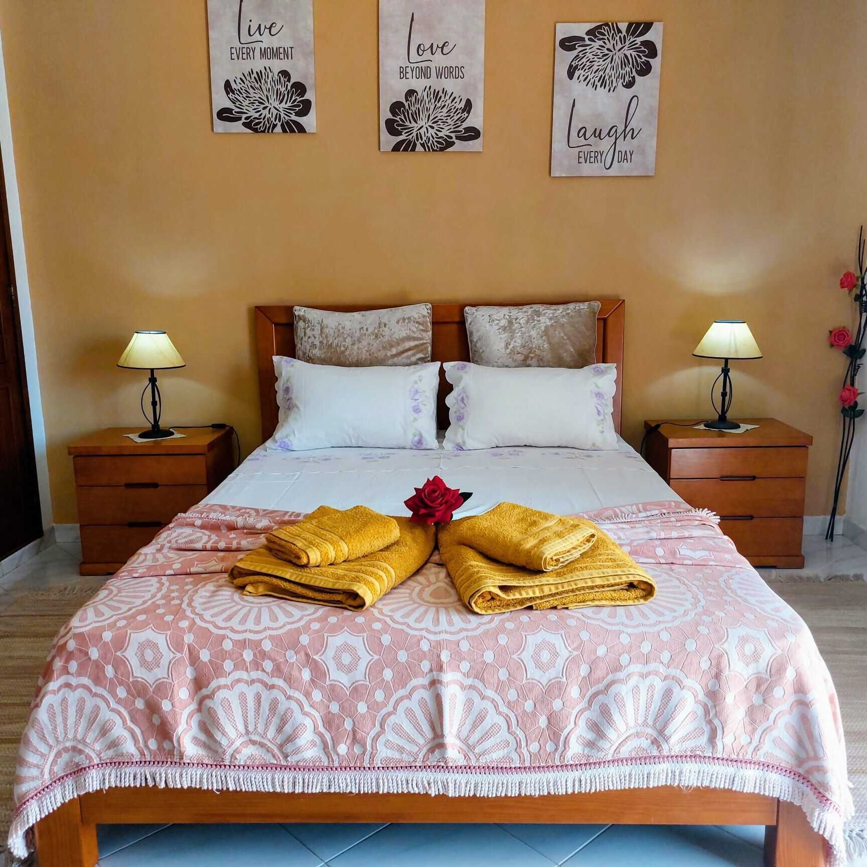 A hotel room with a bed, two bedside tables, a nightstand, a decorative flower, and three wall art pieces.