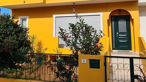 Un edificio amarillo de dos pisos con balcones, una puerta verde y un camino adoquinado.
