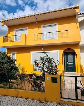 A two-story yellow building with balconies, a green door, and a cobblestone pathway. - Ria Formosa Pineview (Faro)